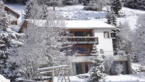 Un rifugio alpino innevato con una veranda in legno, un balcone e una seggiovia.