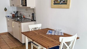 Una piccola cucina con tavolo in legno e sedie bianche, una parete rivestita di piastrelle e un forno a microonde.