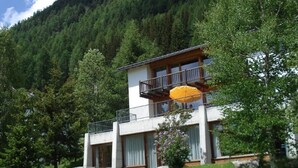 Un edificio a due piani con un balcone, immerso nel verde e con vista sulle montagne.