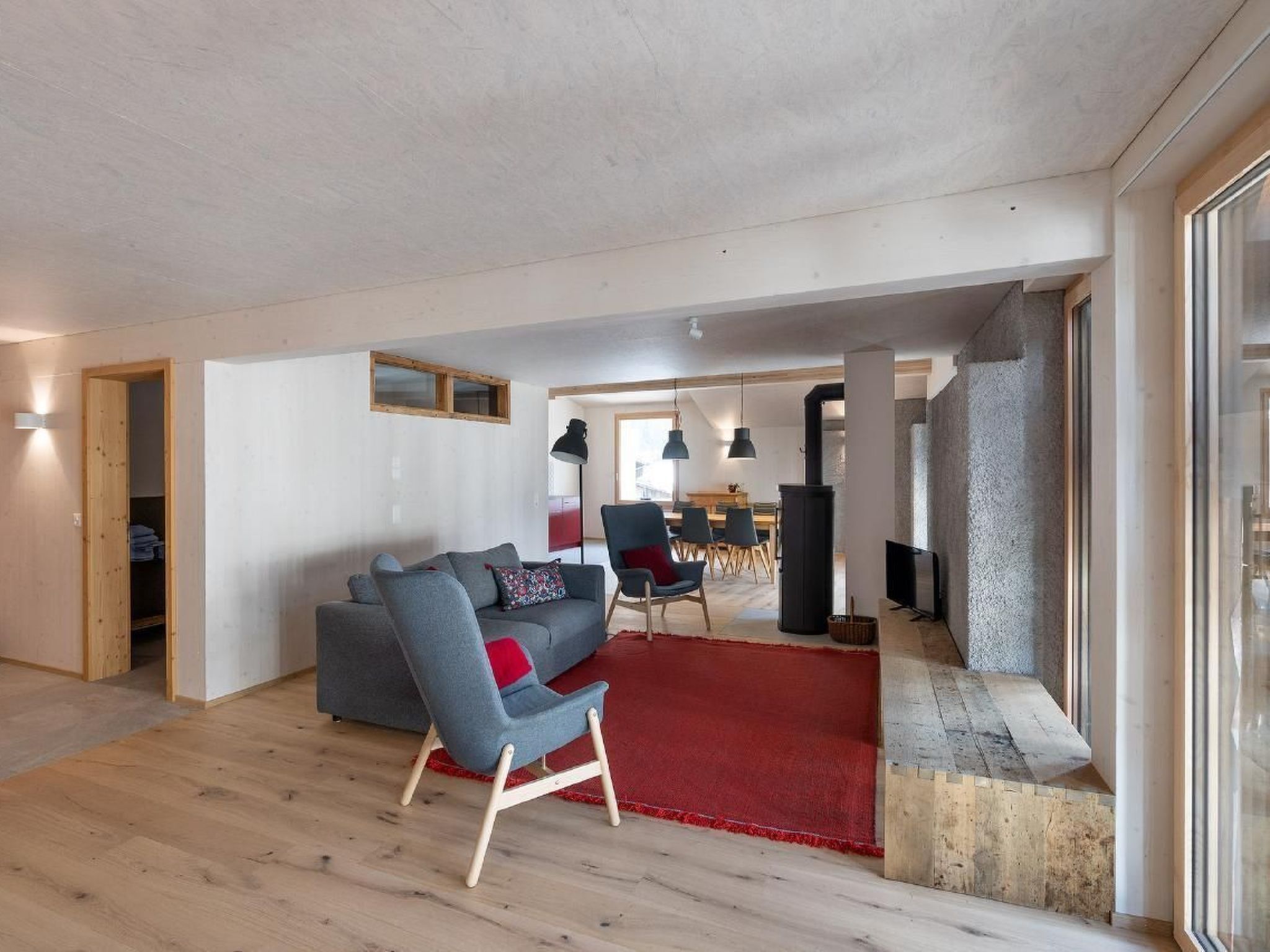 Un salon moderne avec un canapé gris, un tapis rouge et un plancher en bois.