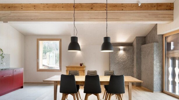 A modern dining area with a wooden table and black chairs, a red cabinet, and a large window with a view of a building. - Bellezza - Bio Bergün by Interhome (Bergün)