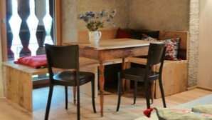 Un comedor acogedor con una mesa y sillas de madera, un florero con flores y un banco con cojines.