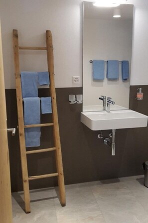Ett badrum med en trästege, ett vitt handfat och två blå handdukar som hänger på väggen.