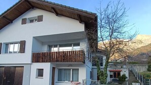 Un edificio residencial de dos plantas con un balcón, un pequeño espacio para sentarse al aire libre y vistas a un paisaje montañoso.