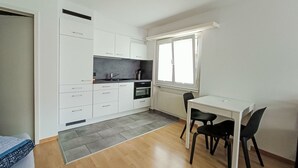 Una cocina moderna con armarios blancos, encimera negra y un comedor con mesa blanca y sillas negras.