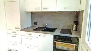 Una cocina compacta con gabinetes blancos, un lavamanos de acero inoxidable y un horno empotrado.