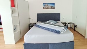 Un dormitorio con cama, mesita de noche, un cuadro en la pared y un armario entreabierto.