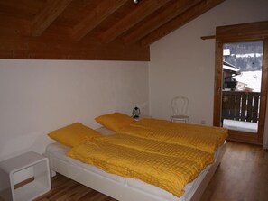 A bedroom with a wooden ceiling, a bed with yellow bedding, a white nightstand, and a chair. - Casa Sagogn Laax by Interhome (Sagogn)