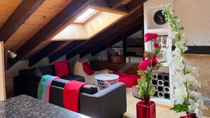 A cozy attic room with a sloped ceiling, a skylight, a sofa, a small round table, and a vase with flowers. - Helle und moderne Dachwohnung by Interhome (Aminona)