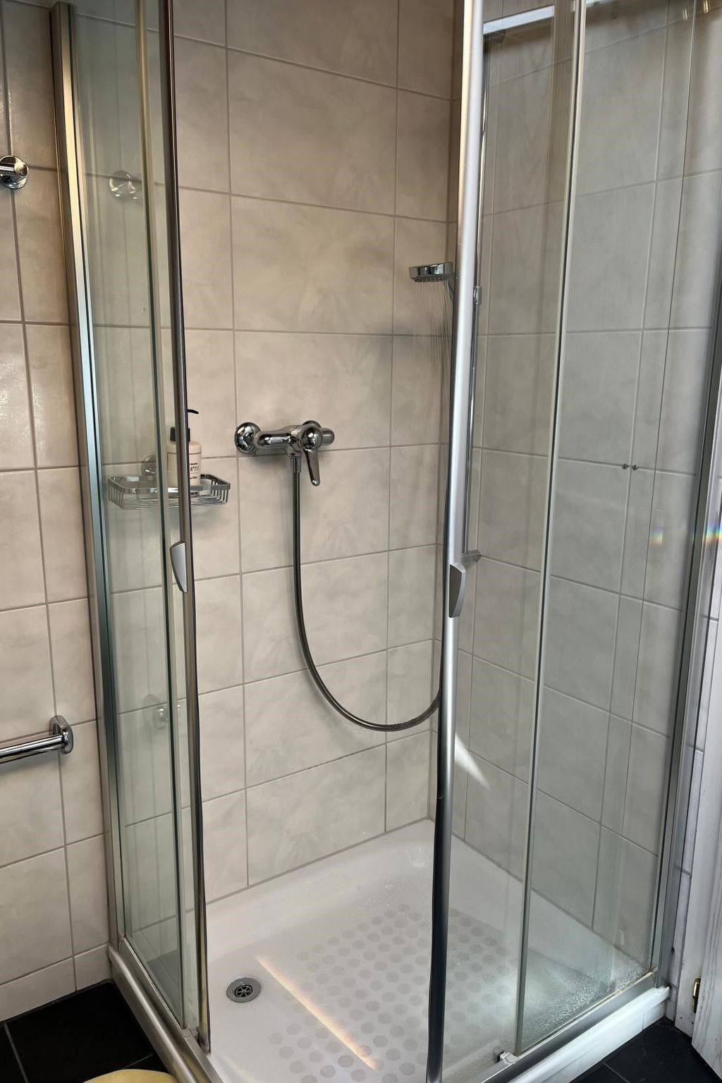 Eine Duschkabine mit Glaswänden, einer Handbrause und einem Bedienhebel.