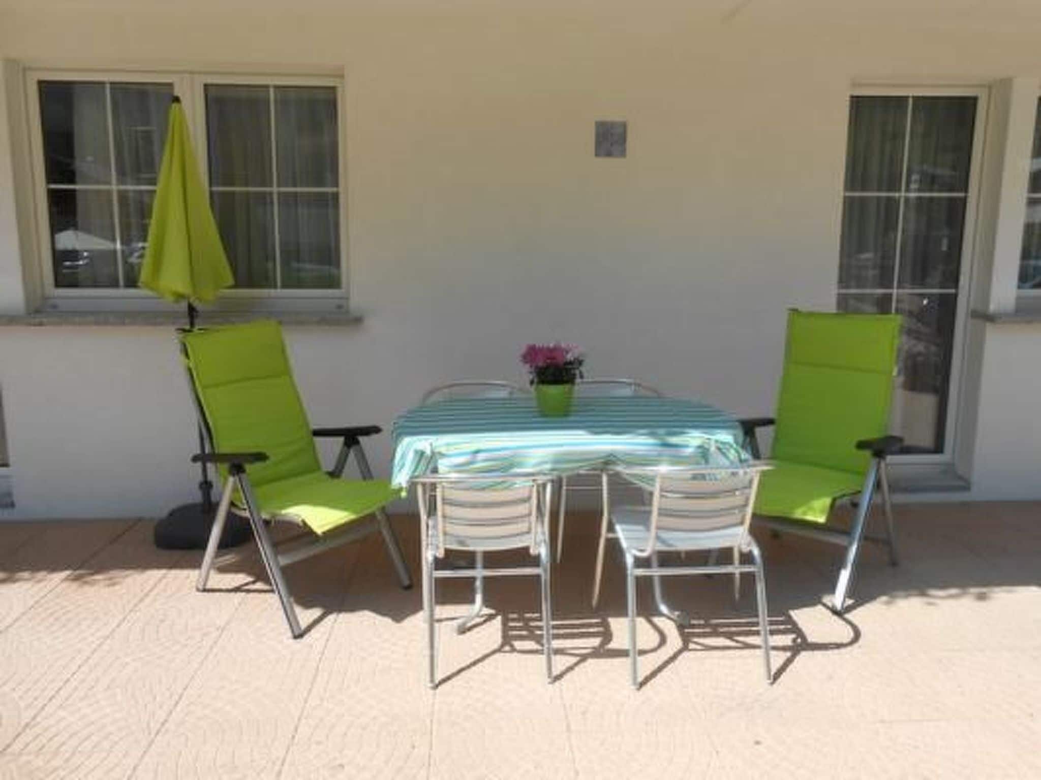 A patio with a table and four chairs, a small potted plant, and a window with a curtain.