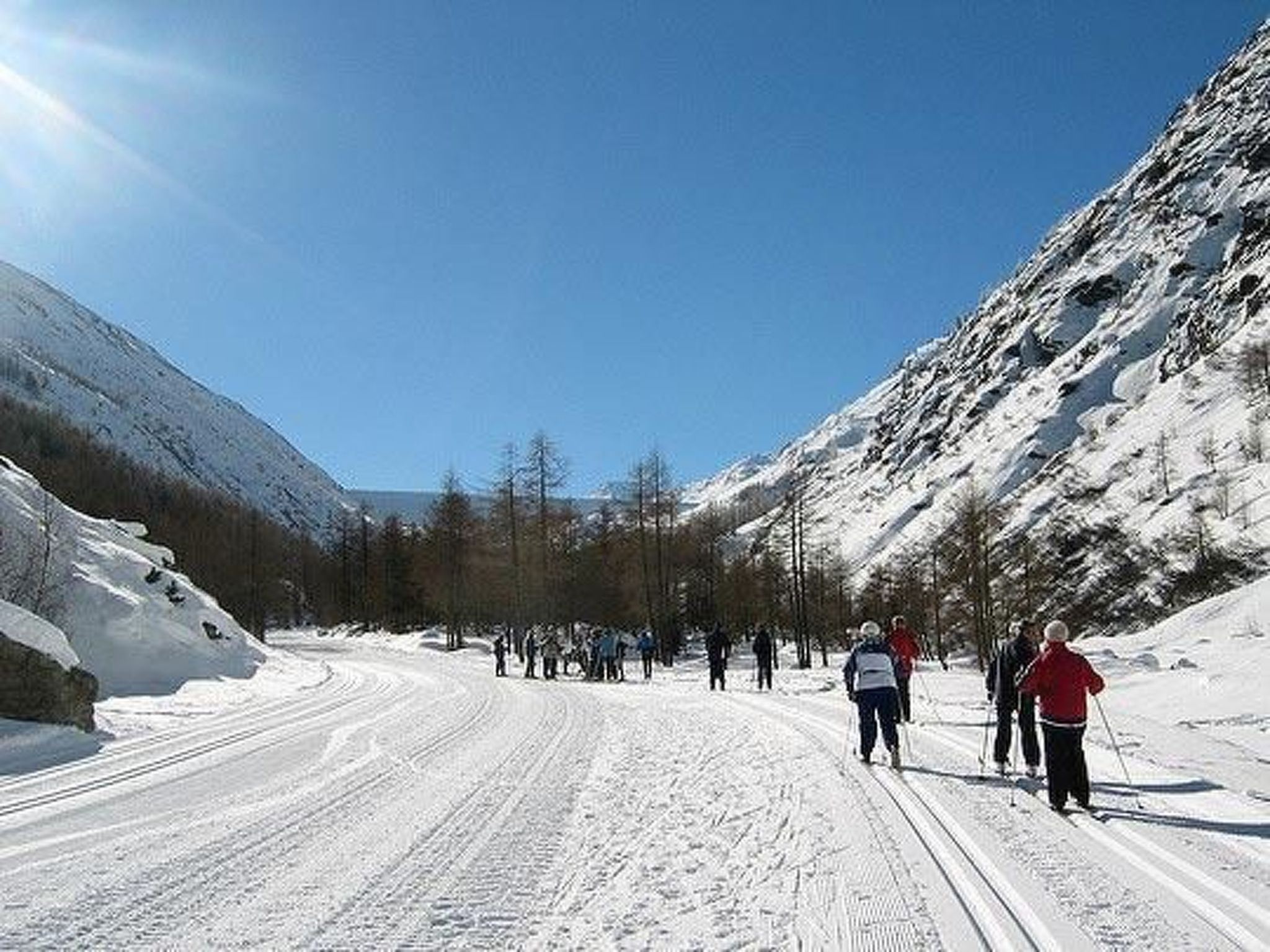 Eine verschneite Bergstraße mit Skifahrern und wolkenlosem, blauem Himmel.
