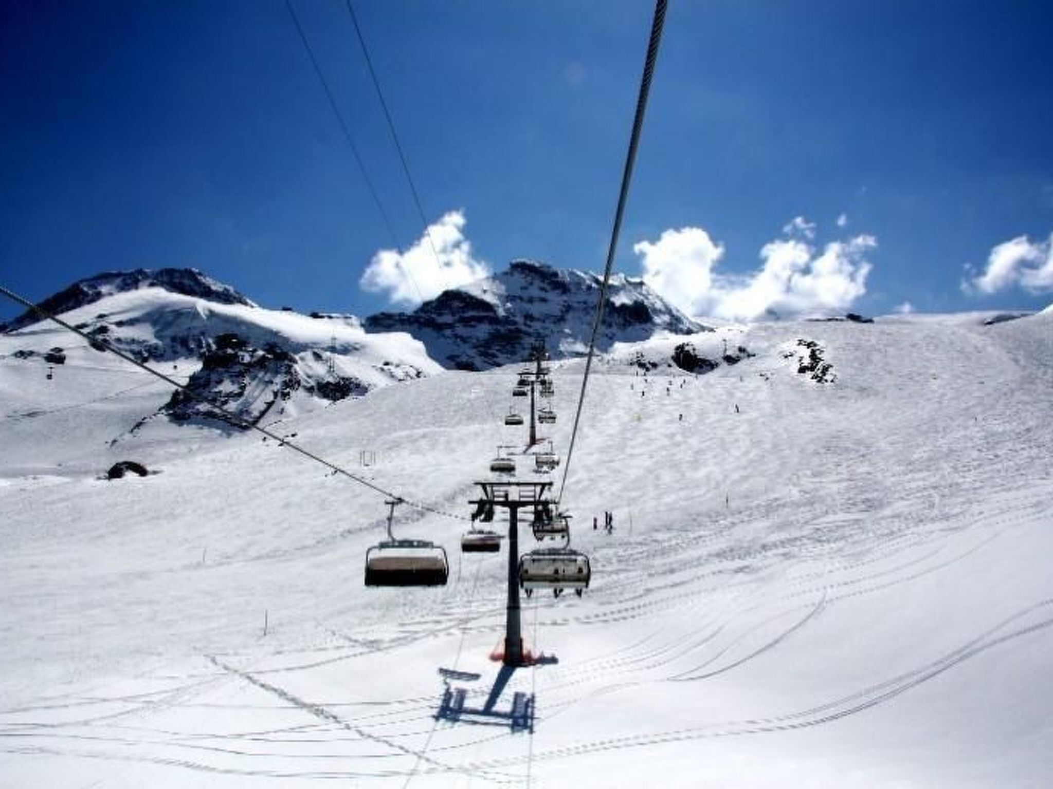 A ski lift with chairs ascending a snowy slope, with mountains in the background.