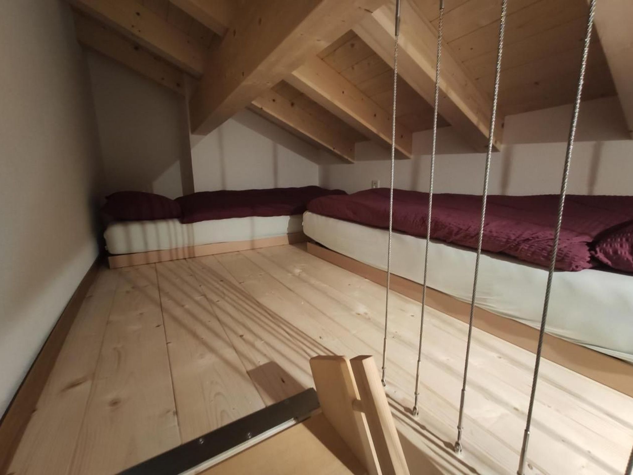 Een slaapkamer in loftstijl met een schuine kap, houten balken en een bed met een wit en paars dekbed.