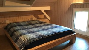 Un dormitorio tipo loft con cama de madera, techo inclinado y ventana.