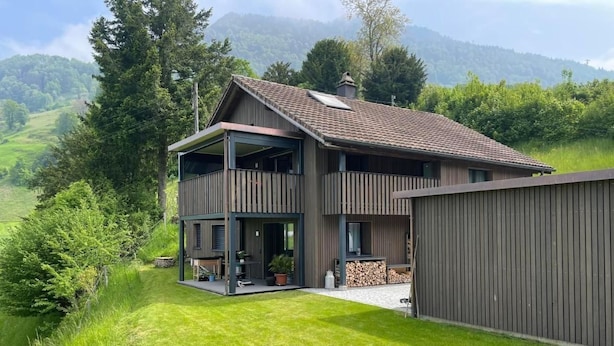 Una casa de dos plantas con un balcón, un porche cubierto y vistas a un paisaje verde.