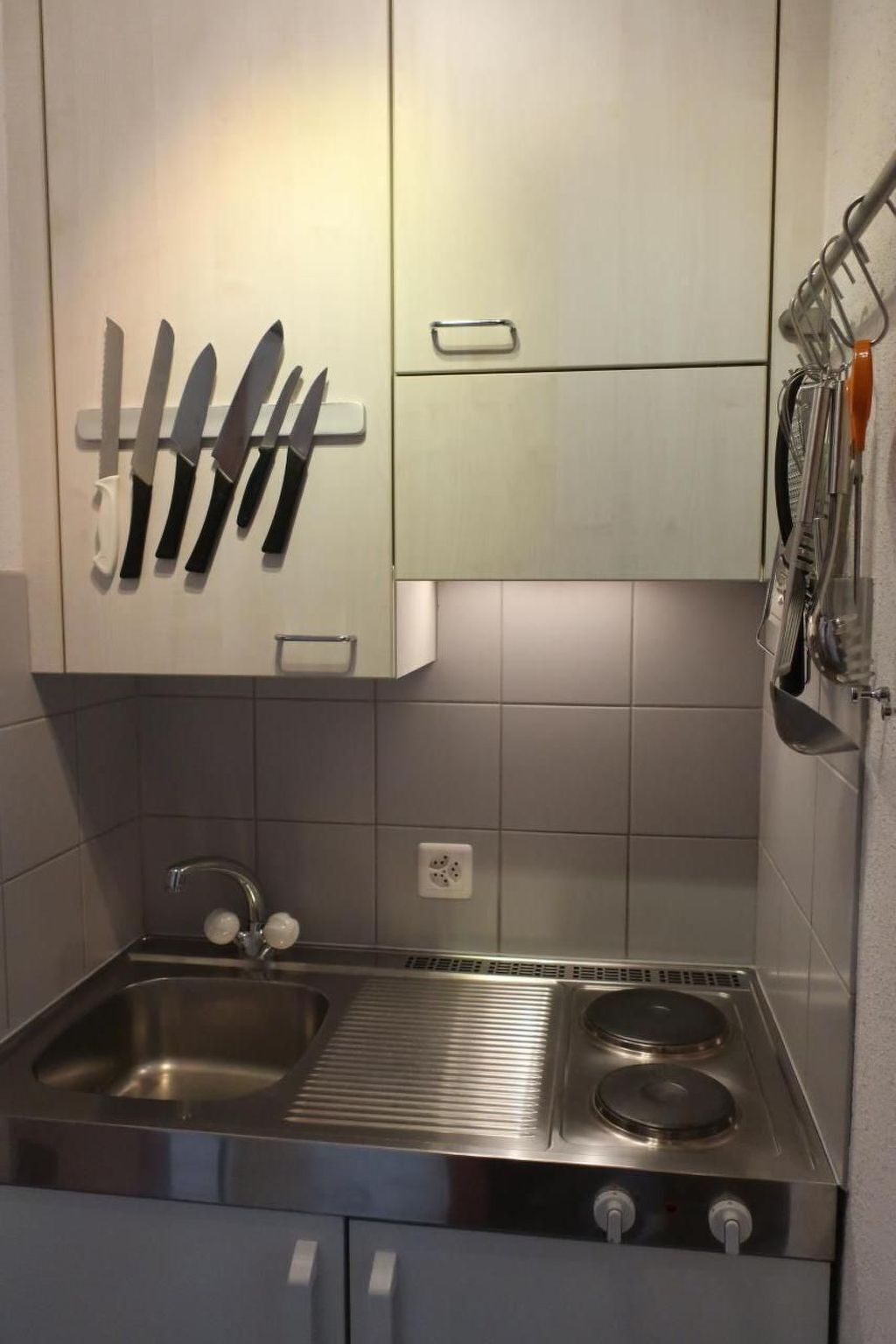 Una cocina con un lavamanos de acero inoxidable, una estufa y cuchillos colgados en la pared.