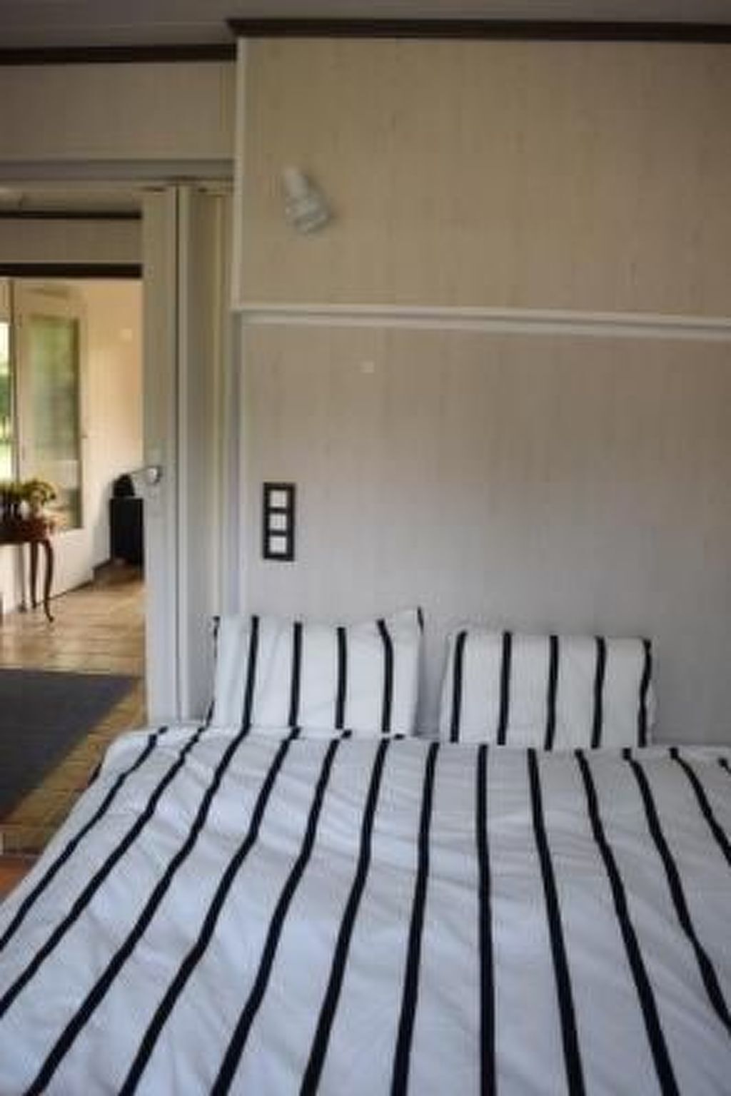 Un dormitorio con una cama grande, una puerta que da a otra habitación y una lámpara fijada a la pared.