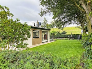 A modern house with a well-maintained lawn, a small garden, and a large tree. - Kleine woning met tuin direct achter de dijk by Interhome (Baarland)