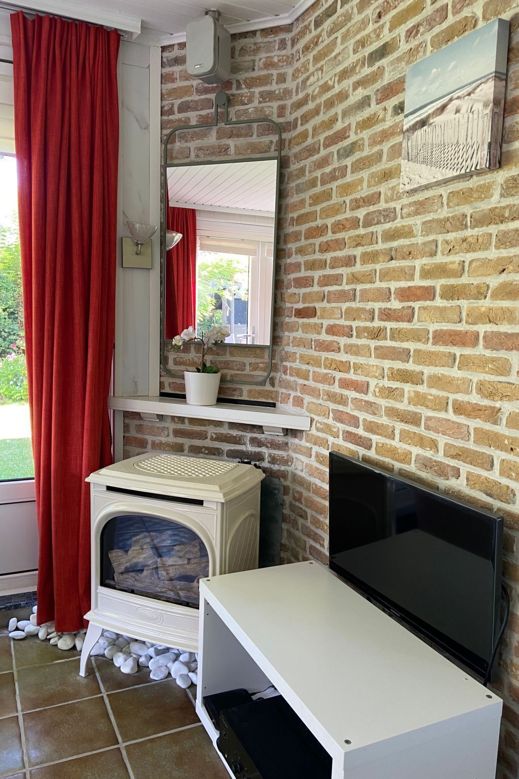 A room with a brick wall, a white cabinet, a TV, and a red curtain.
