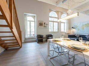 Un comedor moderno con una escalera de madera, una mesa para cuatro personas y un sofá al fondo.