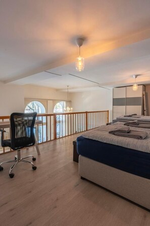Un dormitorio amplio con una cama grande, un escritorio y una silla. Tiene un balcón con barandilla y vistas a árboles.