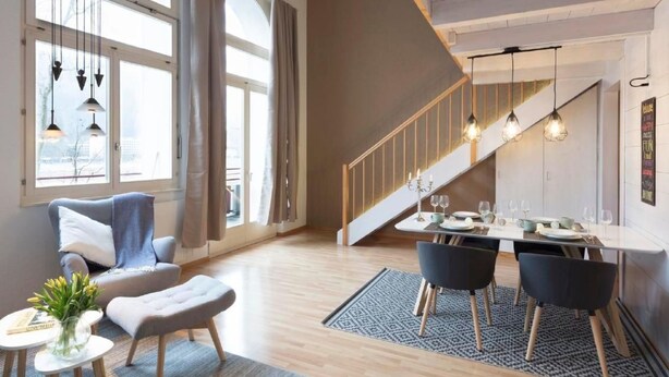 Ein modernes Wohnzimmer mit Essbereich, großen Fenstern und einer Treppe.