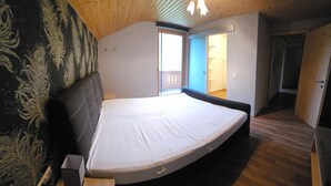 Ein Schlafzimmer mit Bett, Holzboden und Blick auf einen Balkon.