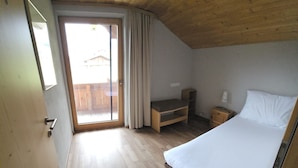 Ein Schlafzimmer mit einem Bett, einem Nachttisch, einer hölzernen Bank und einer Schiebetür zu einem Außenbereich.