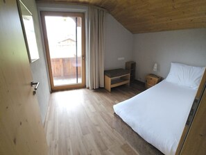 Ein Schlafzimmer mit einem Bett, einem Nachttisch, einer hölzernen Bank und einer Schiebetür zu einem Außenbereich.