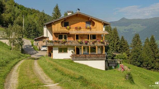 Eine zweistöckige Holzhütte mit Balkon, umgeben von üppiger Vegetation und Bergen.