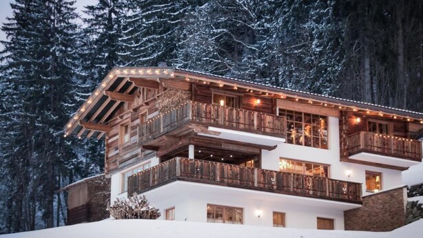Una cabaña de madera de varios pisos con balcones, rodeada de árboles cubiertos de nieve.