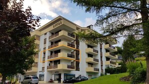 A multi-story hotel named "ROYAL" with balconies, a parking area, and a grassy slope. - Royal 22 nahe Klinik, Burgerbad, Einkaufszentrum by Interhome (Leukerbad)