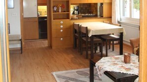 A compact kitchen with wooden cabinets, a dining table, and a window providing natural light. - Royal 22 nahe Klinik, Burgerbad, Einkaufszentrum by Interhome (Leukerbad)