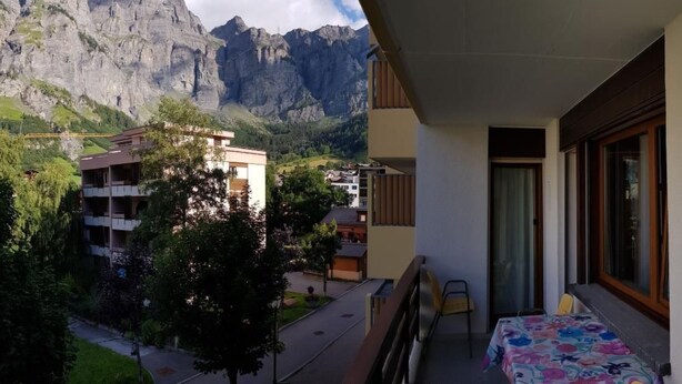 A balcony with a mountain view, a dining area with a table and chairs, and a bed with a floral bedspread. - Royal 22 nahe Klinik, Burgerbad, Einkaufszentrum by Interhome (Leukerbad)