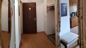 A hallway with a wooden floor, a door with a number, a coat rack, a chair, and a kitchen area visible through an open door. - Royal 22 nahe Klinik, Burgerbad, Einkaufszentrum by Interhome (Leukerbad)