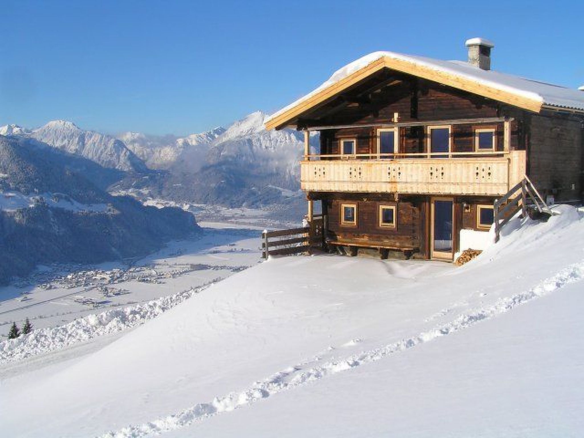 A wooden chalet with a balcony, set against a snowy mountain backdrop.