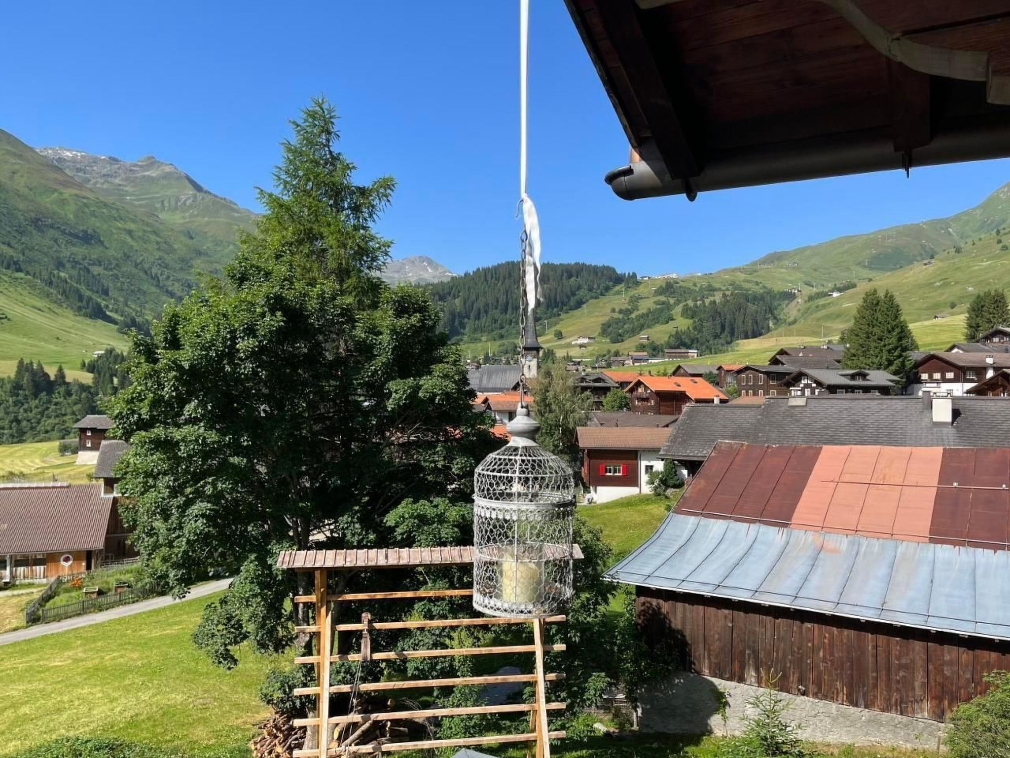 Un village rural avec des maisons traditionnelles en bois, un grand arbre et une mangeoire à oiseaux.