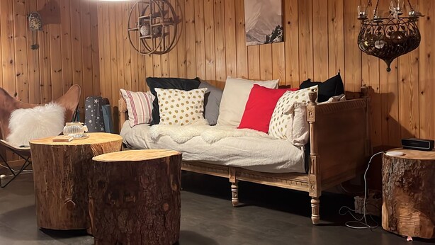 A cozy room with a wooden wall, a bed with patterned pillows, a hanging light fixture, and a rustic wooden table. - mit Bergblick by Interhome (Rueras Dieni)