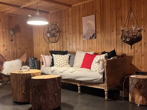 Tunnelmallinen huone, jossa on puuseinä, kuviollisilla tyynyillä varustettu sänky, riippuvalaisin ja maalaishenkinen puupöytä.
