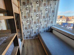 Una habitación con techo inclinado, una ventana que da a vista de edificios y una pared decorada con matrículas antiguas.
