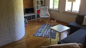 Ett mysigt vardagsrum med ett träpanelat tak, en vit soffa, ett litet bord och en lekmatta med siffror.
