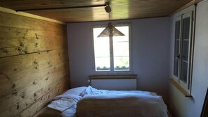 Ett litet rum med en enkel säng, träpanel på väggarna, ett fönster med en hängande lampa och ett element.