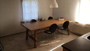 En matplats med ett träbord, sex stolar, en hängande taklampa och ett fönster med gardiner.