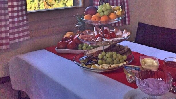 Una mesa de comedor con una tabla de quesos y frutas, una copa de postre y vistas a las montañas a través de una ventana.