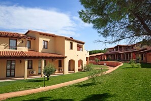 A courtyard with a building featuring arched doorways and a tiled roof. - Olivastro Apartment Ac Wifi, Gallura (Vignola)