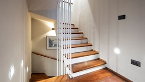 Eine Treppe mit Holzstufen und weißen Geländern, die zu einer Empore mit einem gerahmten Bild führt.