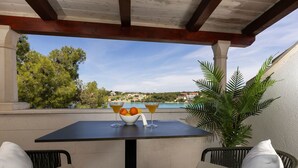 Eine Terrasse mit Tisch, zwei Korbstühlen, einer Obstschale und einem Glas.