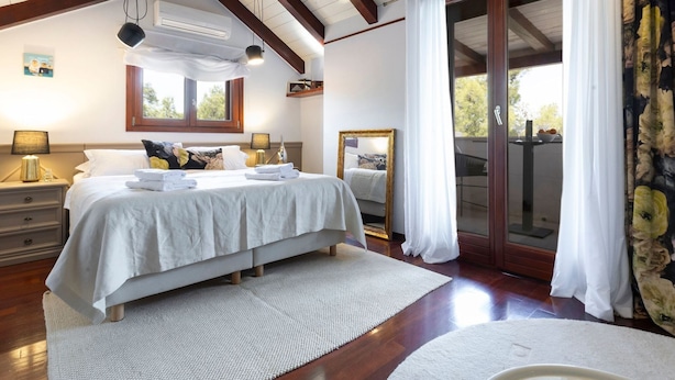 Ein Schlafzimmer mit einem großen Bett, einem Fenster, einem Spiegel und Blick ins Freie.