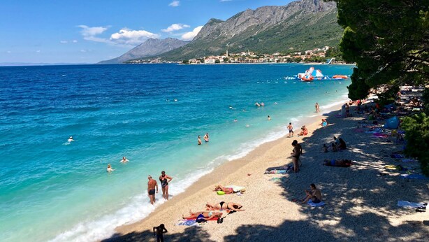 A beach with clear blue water, people swimming and sunbathing, and a mountainous backdrop. - mit privatem Parkplatz by Interhome (Gradac)